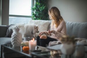 A woman sits with her dog on the couch in her living room.