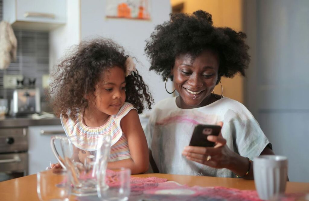 Mother and daughter sit in kitchen looking at phone happily