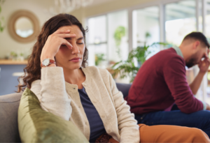 Woman and man facing away from each other on sofa, with their hands on their foreheads in frustration.